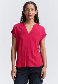 Kurzärmliges V-Ausschnitt-Shirt in leuchtendem Pink. Aus weichem, leichtem Stoff mit lockerer Passform und umgeschlagenen Ärmelabschlüssen.
