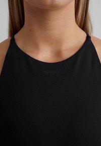 Črn športni top z visokim ovratnikom in tankimi trakovi. Ima logo vtisnjen na prsih. Gladka tekstura, oprijet dizajn.