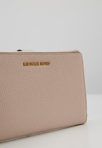 Pink leather wallet with a textured finish, featuring a gold "MICHAEL KORS" logo and a zip closure along the top edge.