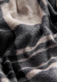 Weiche, strukturierte Decke mit einem abstrakten Muster in Schwarz, Grau und Beige, die Falten und eine plüschige Oberfläche zeigt.