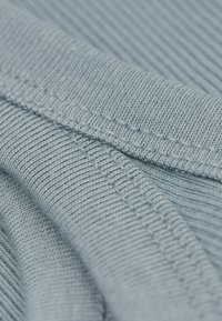 Světle modrá ribbovaná látka s jemnou strukturou, obsahující těsně umístěné rovnoběžné pruhy a úhledné stehy podél okrajů.