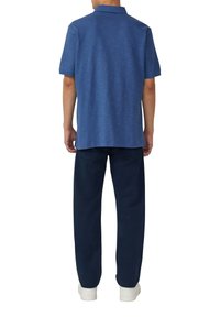 Niebieska koszulka polo z teksturowanym wzorem, z krótkimi rękawami i kołnierzykiem, w zestawieniu z granatowymi spodniami i białymi sneakerami.