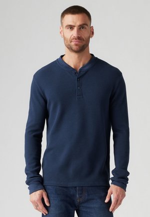 Donkerblauw ribbelachtig langemouwen shirt met een henley-kraag en een drieknoopsluiting, gecombineerd met een gestructureerde stof en aansluitende mouwen.