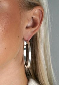 Silverörhänge som visas på ett öra, med en slät, reflekterande yta, rund form och en tunn, solid design.