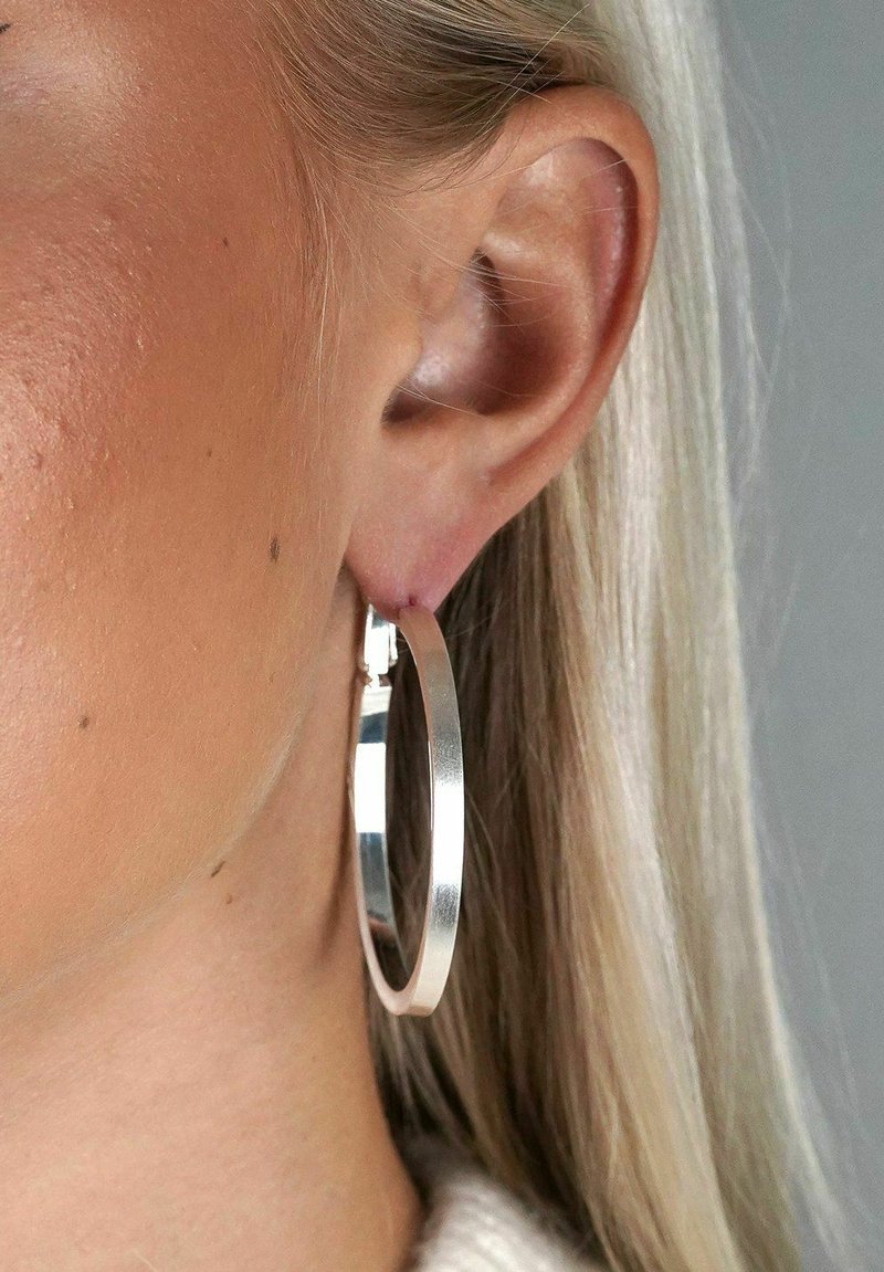 Silverörhänge som visas på ett öra, med en slät, reflekterande yta, rund form och en tunn, solid design.