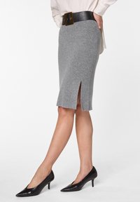 Grauer Strickbleistiftrock mit einem Schlitz vorne, kombiniert mit einem schwarzen Ledergürtel mit goldener Schnalle und schwarzen spitzen Absatzschuhen.