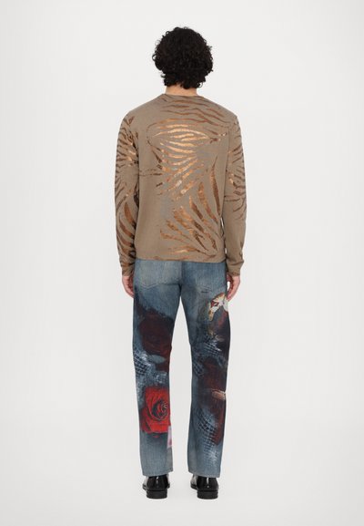 Brown long-sleeve shirt with metallic striped pattern; blue jeans featuring large floral graphics in red and gray; black shoes.
