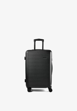 Valigia rigida nera con scanalature orizzontali, manico telescopico estratto e quattro ruote girevoli su sfondo bianco.
