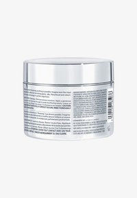 Silver cylindrisk behållare med ett spegelblad, prydd med produktetikett på flera språk som detaljerar instruktioner och ingredienser på en glansig bakgrund.