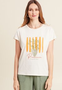 Chemise blanche à manches courtes présentant un graphique d'un vase vert avec des branches d'olivier et des rayures orange, avec le texte "Provence" en dessous.