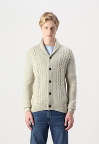Cardigan en maille torsadée crème avec col châle, boutons sur le devant et ourlet côtelé. Associé à un jean en denim, tissu texturé et chaud.