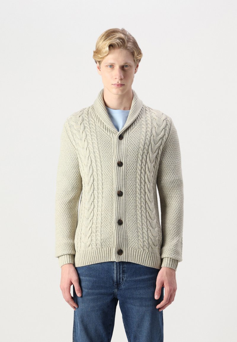 Cardigan en maille torsadée crème avec col châle, boutons sur le devant et ourlet côtelé. Associé à un jean en denim, tissu texturé et chaud.
