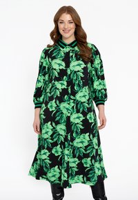 Blumenhemdkleid in Schwarz mit lebhaftem grünen Blatt- und Blumenmuster. Verfügt über eine Knopfleiste, einen Kragen und gestreifte Akzente an den Manschetten.