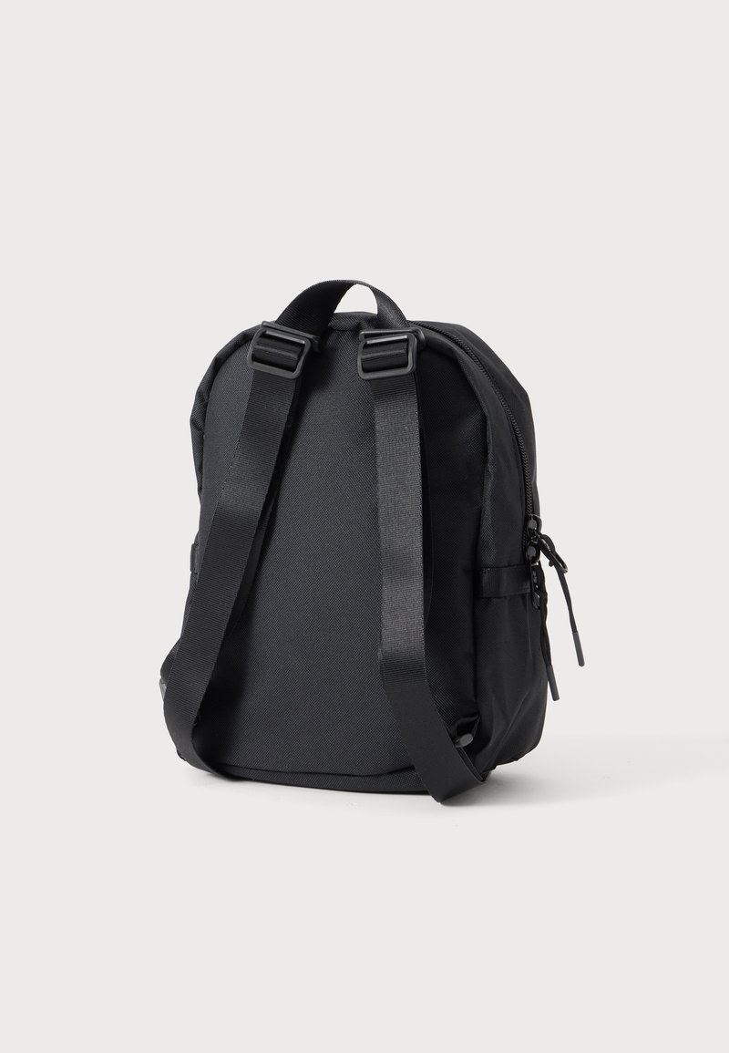 Zaino compatto nero con spallacci regolabili, maniglia superiore e scomparto principale con cerniera su sfondo chiaro uniforme.