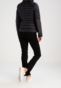 Doudoune noire avec coutures horizontales, manches grises et col montant. Jean noir et baskets blanches complètent la tenue.