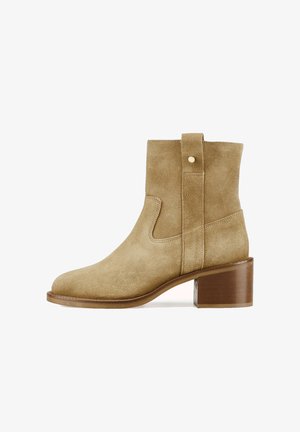 Bottine beige en daim avec un bout arrondi, des découpes latérales et un talon bloc. Elle est dotée d'une languette arrière et d'un détail en métal doré.