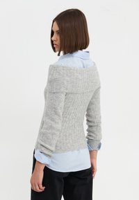 Maglione grigio a coste con design scollato, abbinato a una camicia azzurra con colletto sotto, pantaloni neri e maniche lunghe.