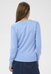 Pull tricoté bleu clair à manches longues, avec poignets et ourlet côtelés. Présente des épaules bouffantes et un col rond.