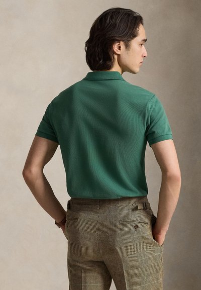 Polo em algodão verde escuro com mangas curtas, apresentando uma gola clássica. Combinado com calças aos quadrados em tons bege e castanho.