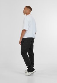 Witte oversized T-shirt, zwarte denim jeans met rechte snit, en witte atletische schoenen. Eenvoudig ontwerp, zachte stof, minimalistische stijl.