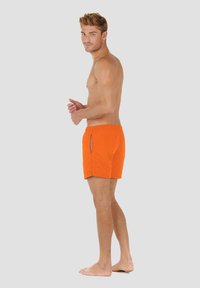 Oranssi uima-asu, jossa on naru vyötärö ja sivutaskut, valmistettu kevyestä materiaalista, yksinkertainen, kuvioton muotoilu.