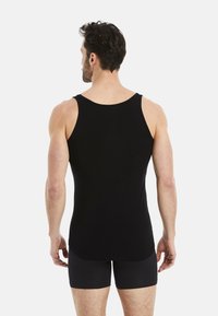 Black tank top made of stretchy fabric, featuring a round neckline and wide shoulder straps, paired with dark fitted shorts.