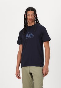 Kleita zila kokvilnas T - krekls ar īsām piedurknēm, ar lielu, reljefa Quiksilver logotipu zila krāsā uz priekšpuses. Klasiska apaļa kakla izgriezuma forma.