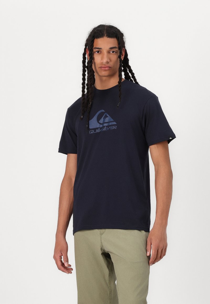 Kleita zila kokvilnas T - krekls ar īsām piedurknēm, ar lielu, reljefa Quiksilver logotipu zila krāsā uz priekšpuses. Klasiska apaļa kakla izgriezuma forma.