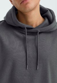 Grijze hoodie van een textuurstof, met een trekkoordkap en een geribbelde halslijn. Minimalistisch ontwerp zonder duidelijke patronen of accenten.