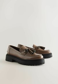 Bruna läderloafers med tjocka svarta gummisulor, med fransar och dekorativt hårdvara. Slät textur med en klassisk design.