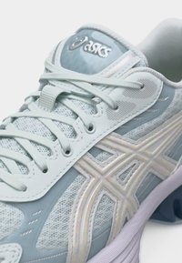 Chaussure de sport ASICS bleu clair et blanche avec dessus en mesh, couture sophistiquée, lacets noués et semelle rembourrée visible.