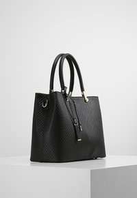 Svart läder tote-väska med diamentriktad ribbad textur, guldfärgad hårdvara, dubbla handtag och en avtagbar rem. Rektangulär botten, strukturerad form.