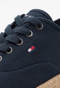 Zapato de lona azul marino con ojales metálicos redondos, cordones de algodón texturizado y suela envuelta en yute. Incluye un pequeño detalle de logotipo tricolor.