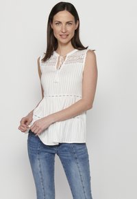 Blusa bianca senza maniche con dettagli in pizzo, design plissettato e chiusura con nodo al collo. Presenta strisce verticali e una vestibilità rilassata.
