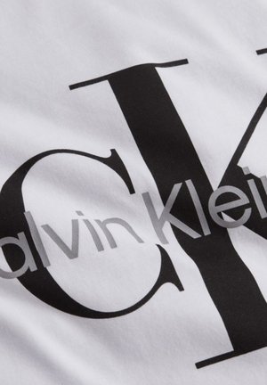 Tissu blanc avec le logo Calvin Klein imprimé en noir et gris, présentant de grandes lettres stylisées "CK" et le nom de la marque par-dessus.