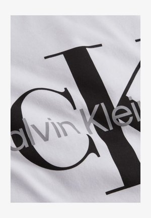 Biely materiál s čierno-sivým vytlačeným logom Calvin Klein, s veľkými štýlizovanými písmenami "CK" a názvom značky cez ne.