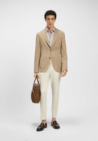 Beige bleiseri, hvor det er spisse lapeller, en lys rutet skjorte, kremfargede bukser og en brun lærveske. Mørkebrune mokasiner fullfører antrekket.