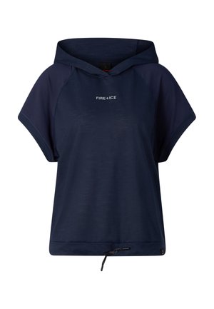 Kobieta stoi, ubrana w granatową bluzę z krótkim rękawem i kapturem, pasujące szerokie spodnie, czarne buty oraz odwróconą granatową czapkę z daszkiem.