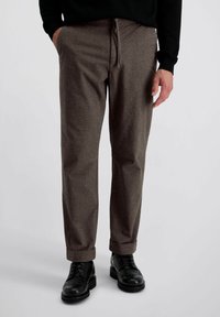 Pantalons texturés gris avec une taille à cordon, jambes droites et ourlets à revers, portés avec des chaussures à lacets noires.