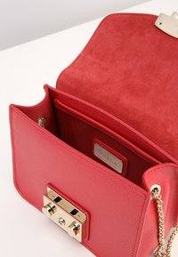 Rote texturierte Lederhandtasche mit goldenen Beschlägen, Klappenverschluss und Wildleder-Innenfutter; verfügt über Innenfächer und eine Kettenriemen.