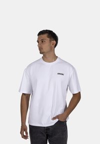 Bílá bavlněná tričko s krátkými rukávy, kulatým výstřihem a černým logem "CRYSTAL" na hrudi. Nosené s tmavými džíny.