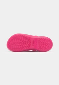 Semelle de Crocs rose vif avec motif de bande de roulement texturé, marquages de taille et logo de la marque visibles, photographiée sur fond blanc.