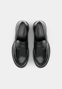 Paire de mocassins en cuir noir avec bouts ronds et détail de bride, nom de la marque "Vagabond" visible à l'intérieur de chaque chaussure.