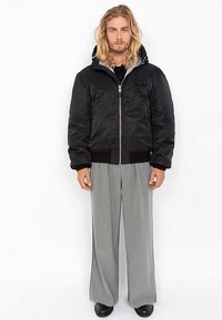 Czarna ocieplana kurtka na suwak z przodu, z kapturem i ściągaczami na rękawach; w zestawie z szarymi, szerokimi spodniami w prążki.