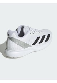 Botte de sport blanche avec un dessus en maille texturée, accents noirs et détails argentés. Dispose d'une semelle rembourrée et d'un système de lacets.