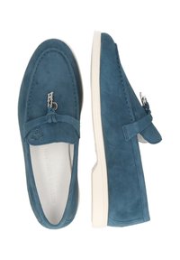 Mocasines de gamuza azul con detalles de herrajes plateados, suela blanca plana y un adorno de borla en la parte delantera.