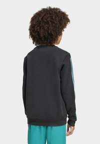 Felpa nera con colletto rotondo, polsini a coste e strisce blu sulle spalle, abbinata a pantaloni azzurri chiari.