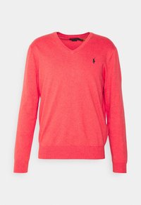 V-ringad, långärmad tröja i ljus korall. Tillverkad av stickat tyg, med ribbad mudd och fåll, samt en liten logotyp på bröstet.