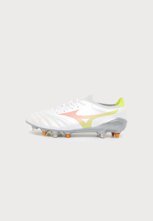 Weißer Fußballschuh mit orange-gelbem Farbverlauf-Logo, weißen Schnürsenkeln und orangen Stollen auf grauer Sohle vor einem schlichten hellen Hintergrund.