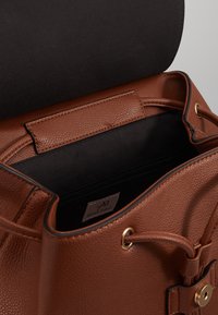 Borsa a tracolla in pelle marrone texturizzata con interno nero, dettagli in metallo dorato e chiusura a pattina. Presenta una tasca con zip all'interno.